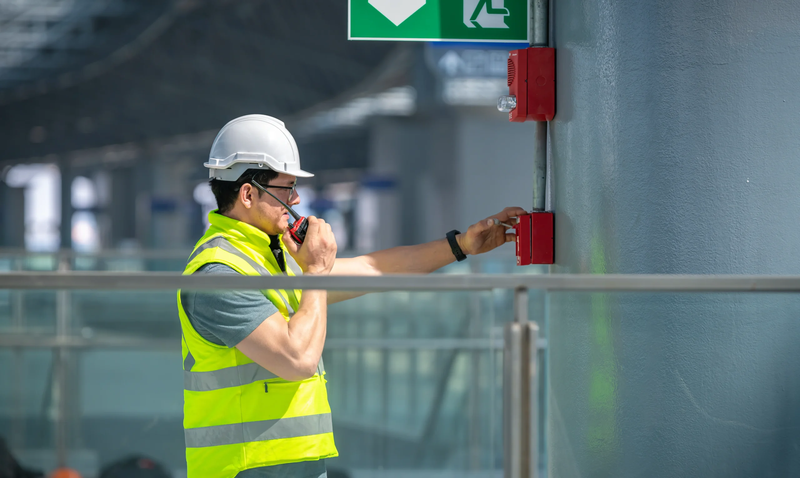 Engineer wearing safety unifrom and helmet under checking fire alarm emergency system in industry factory and exit door is factory security protection concept.