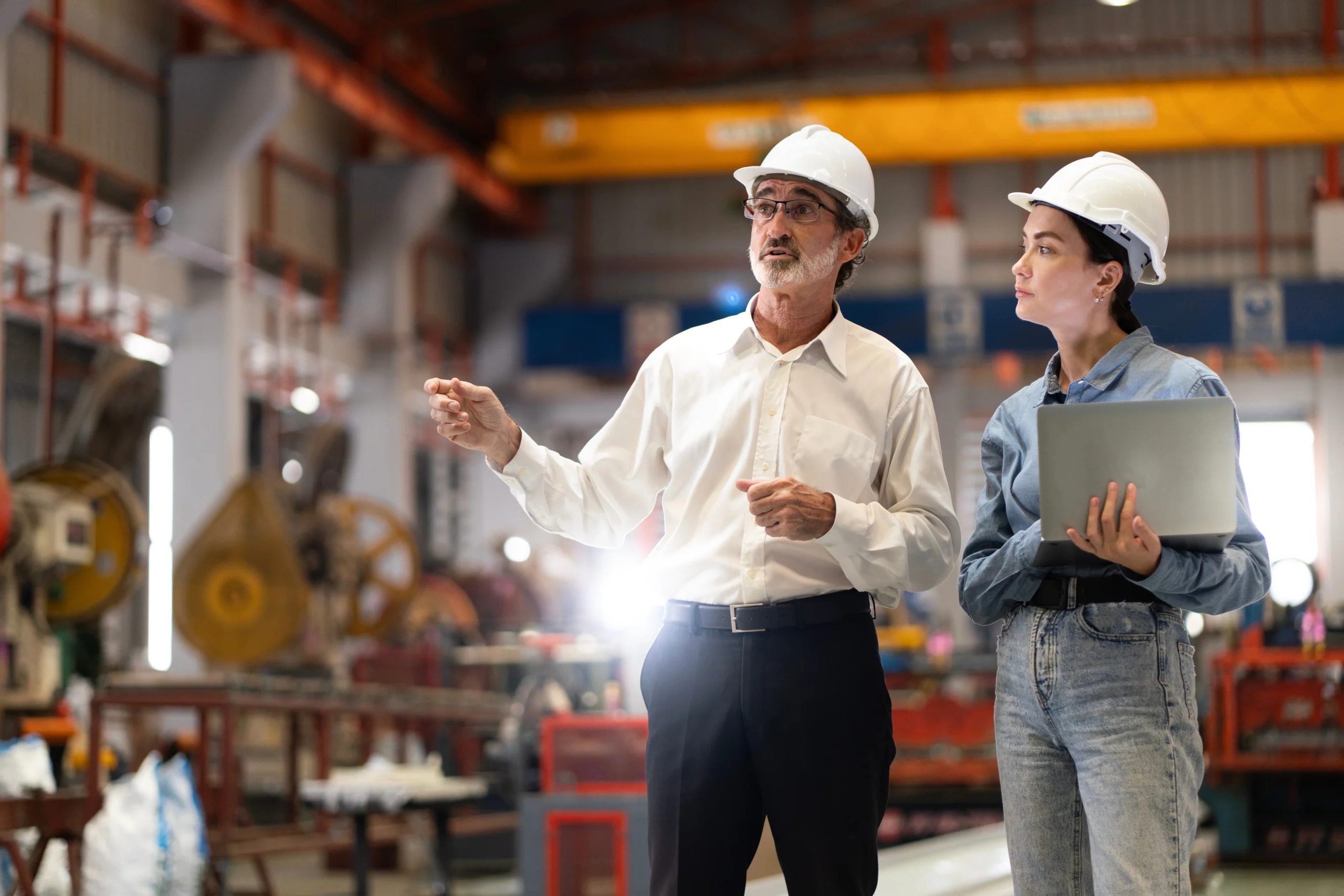 two professional engineer,worker,technician use clipboard discuss work, walk in steel metal manufacture factory plant industry. Black African American man and woman wear hard hat check quality machine