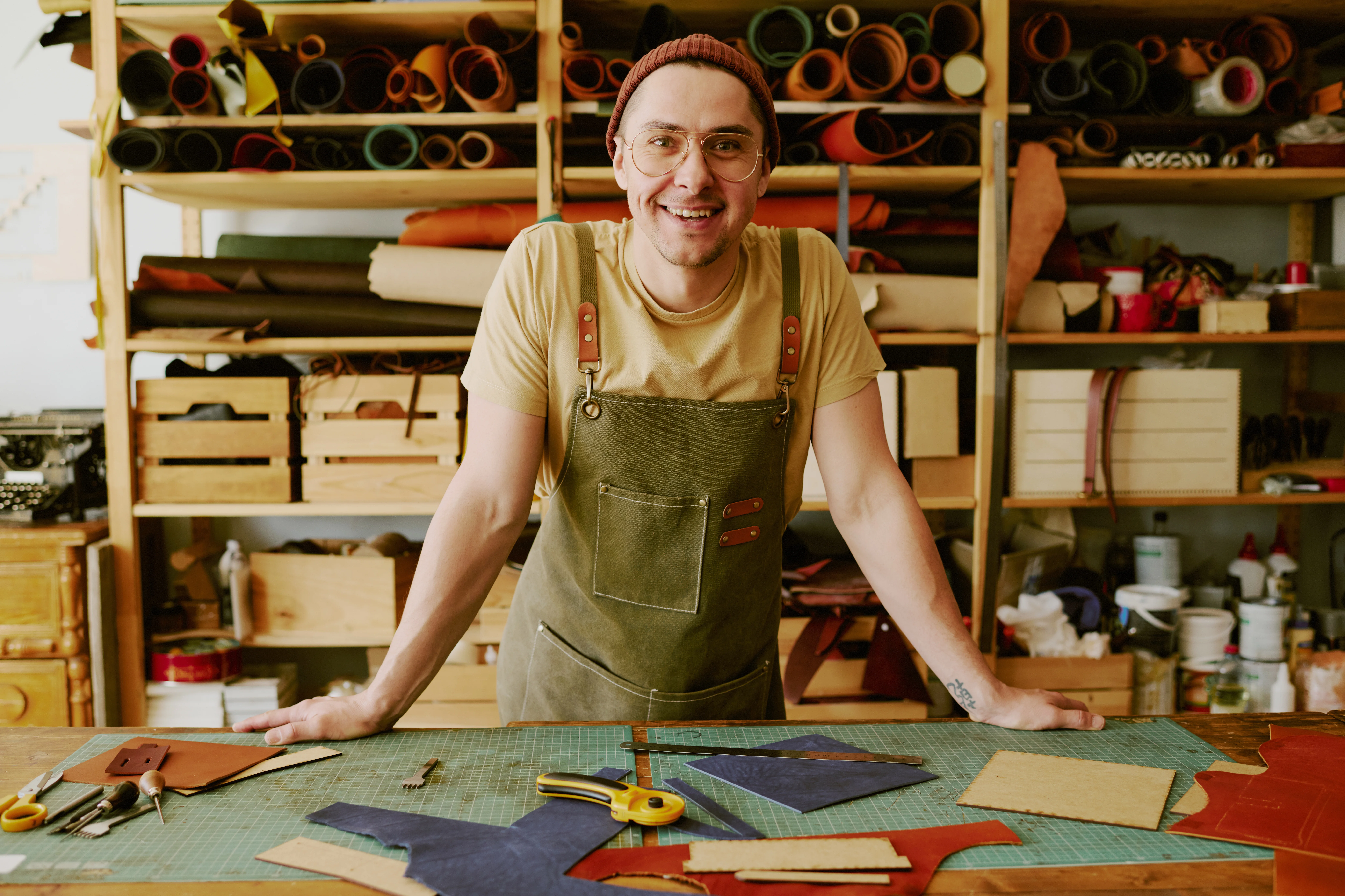 Portrait of young male tailor leaning on antique wooden table in atelier